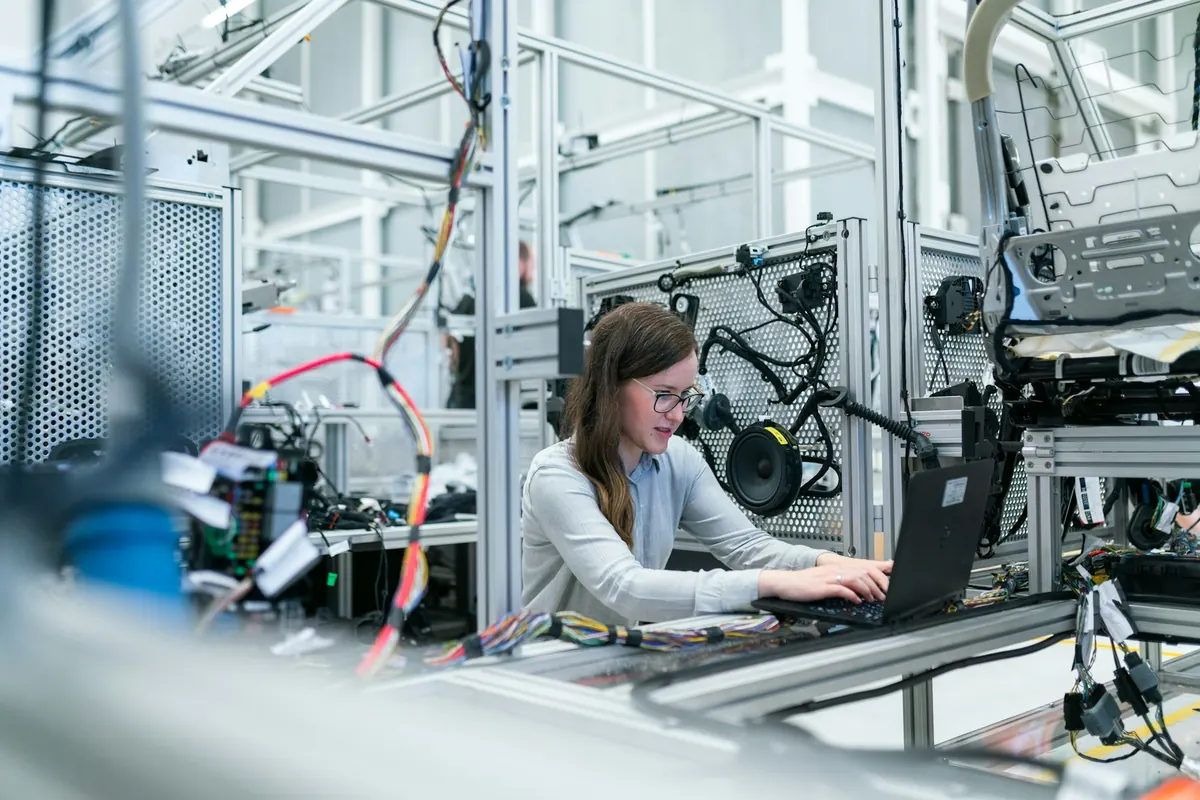 Engineer working at a laptop beside industrial equipment and wiring